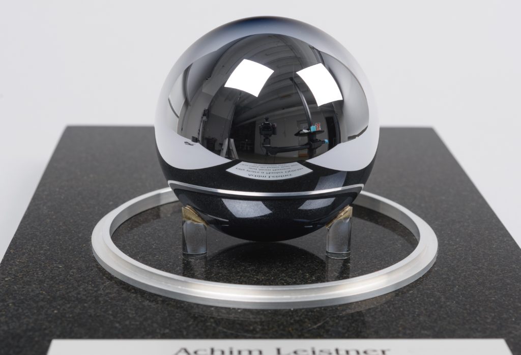Perfectly round silver sphere held by small plastic feet. 